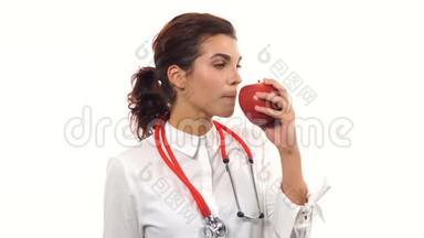 年轻友好的女营养学家<strong>展示</strong>一个红<strong>苹果</strong>，咬它，微笑，建议健康饮食。 青年肖像